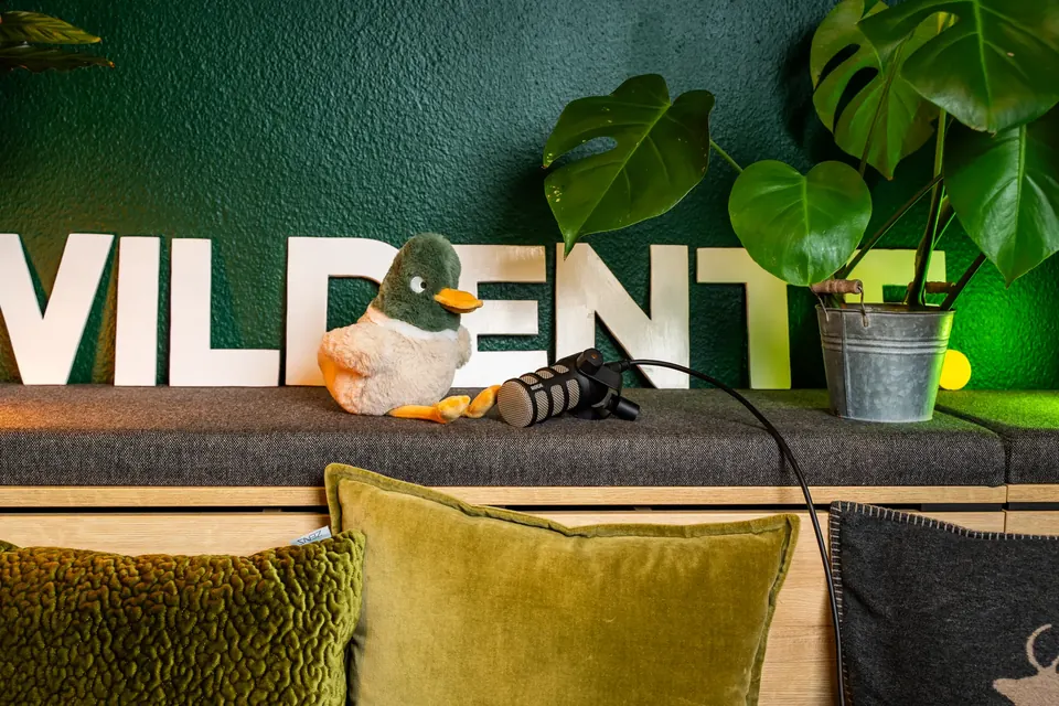 Wildente-Schriftzug mit Enten-Figur auf der Sitzbank vor der grünen Bürowand