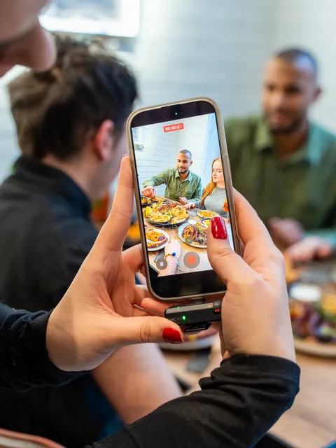 Hand filmt mit dem Smartphone zwei Personen beim Essen für ein Social-Media-Reel