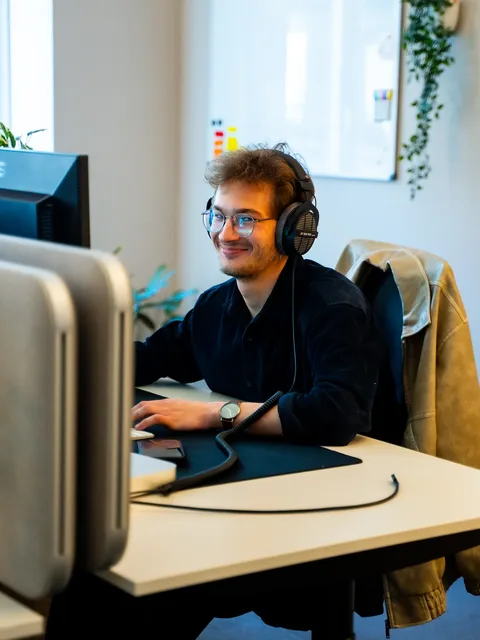 Teammitglied mit Kopfhörern arbeitet konzentriert am Monitor