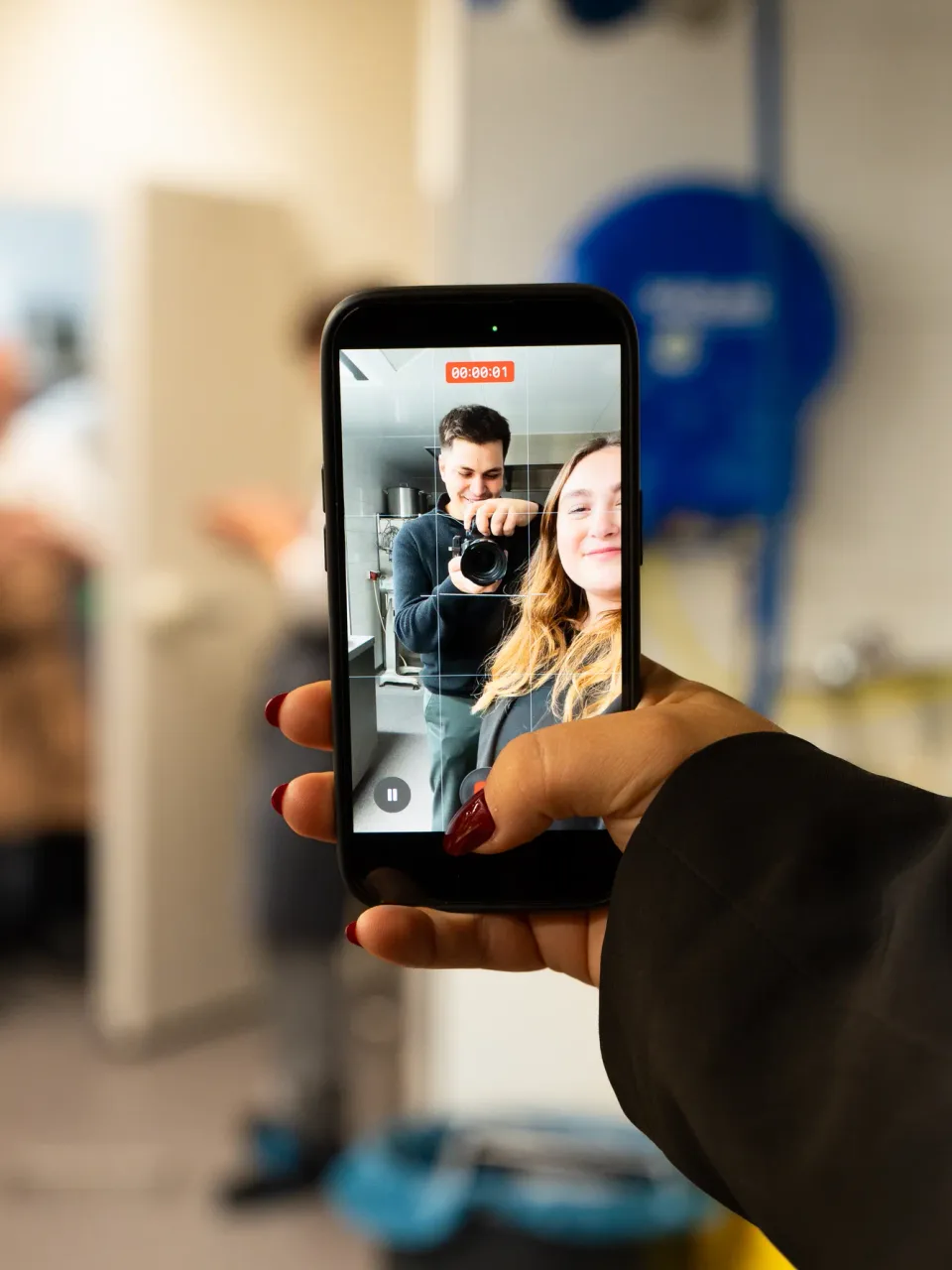 Hand hält Smartphone und filmt zwei Creator beim Dreh eines Reels
