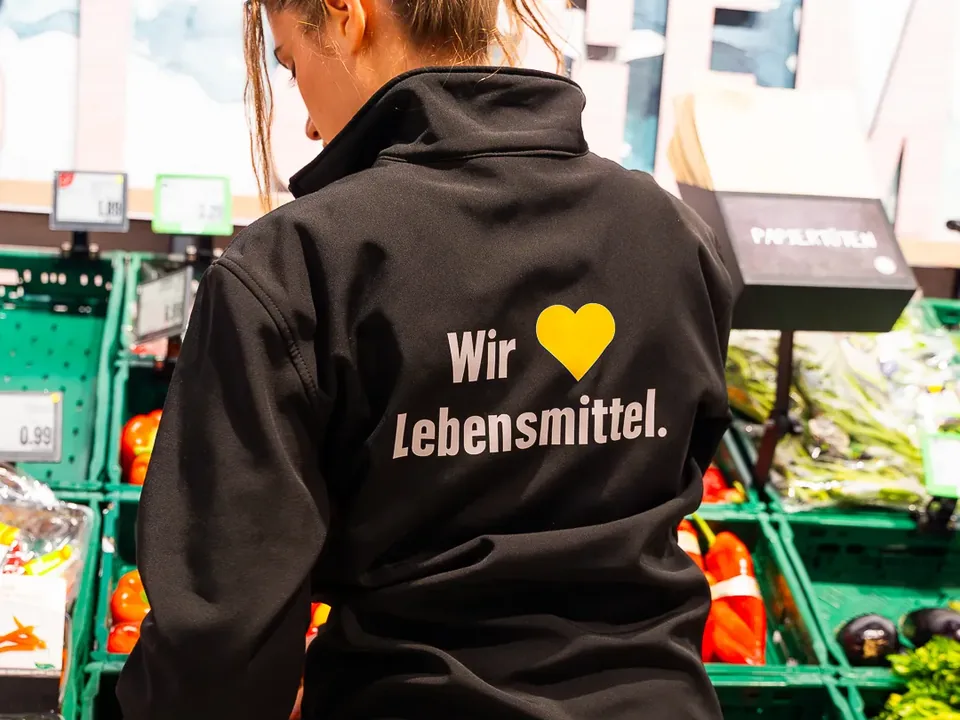 Brandface Lilit von hinten in der „Wir lieben Lebensmittel“-Jacke im EDEKA Fitterer Markt