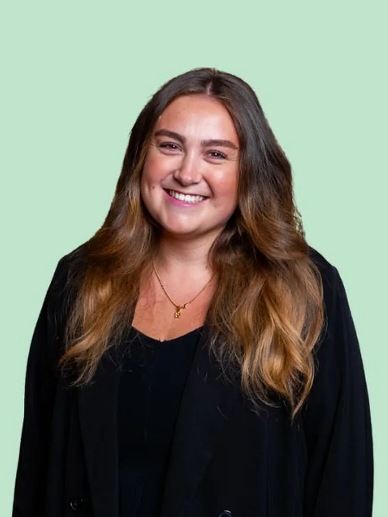Selina im schwarzen Blazer lacht in die Kamera vor mintgrünem Hintergrund